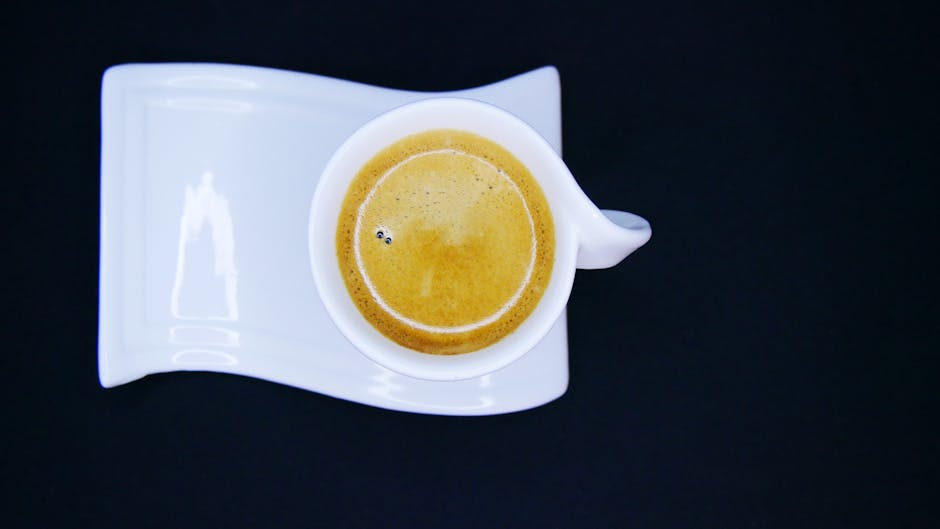 Artistic flat lay of espresso cup on white saucer over black background, showcasing contrast and minimalism.